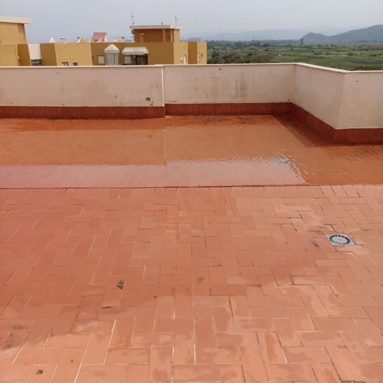 Impermeabilización de cubiertas Terraza de color terracota de un edificio con una zono impermeabilizada y brillante